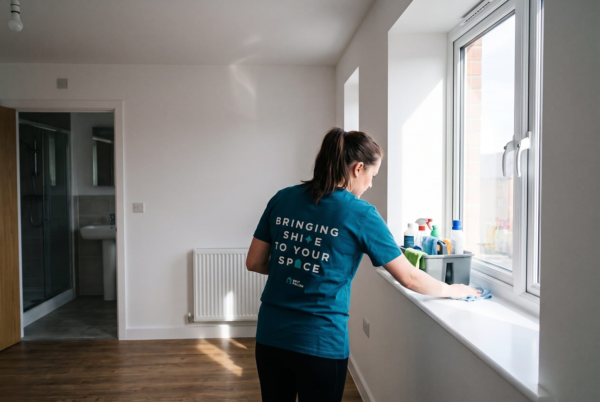 A Brit Polish cleaner wiping down a windowsill in a bright, freshly prepared room